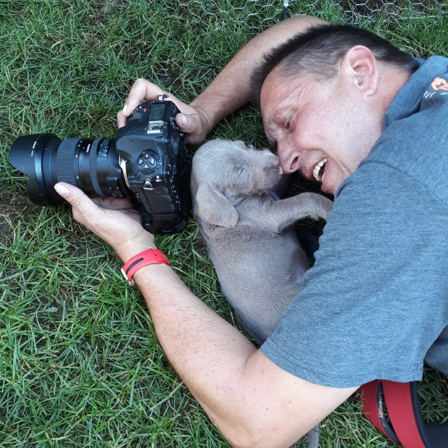 Fotograf liegt auf der Wiese neben einem grauen Welpen, der seine Nase leckt