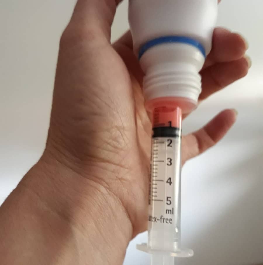 Hand zieht mit einer Spritze Flüssigkeit aus einer auf dem Kopf stehenden Flasche auf