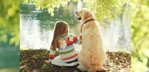 Kind und Hund sitzen nebeneinander an einem see