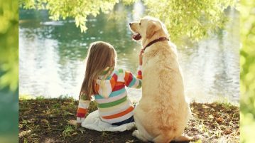 Kind und Hund sitzen nebeneinander an einem see