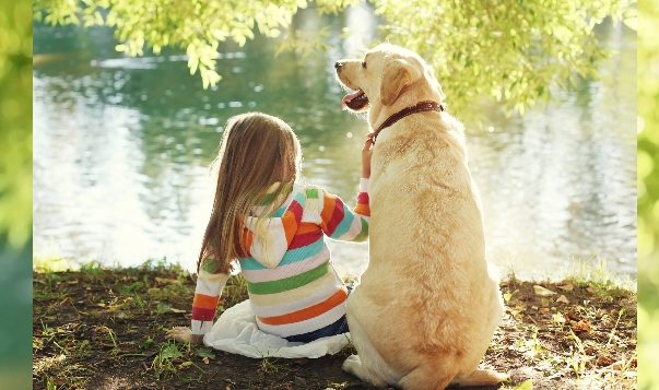 Hunde helfen Kindern, die beim Spracherwerb Schwierigkeiten haben Kind und Hund sitzen nebeneinander an einem see