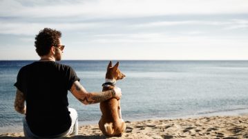 Mann und Hund sitzen am Strand