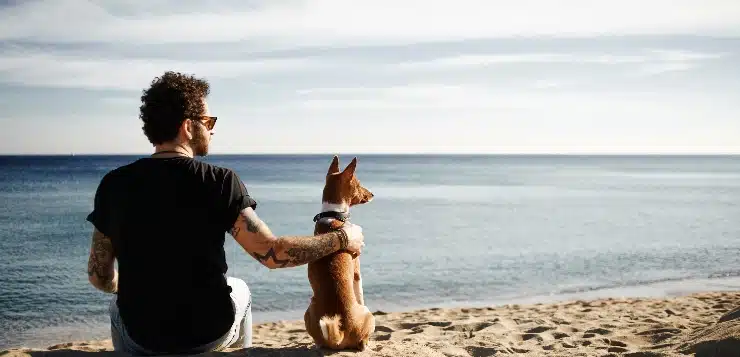 Mann und Hund sitzen am Strand