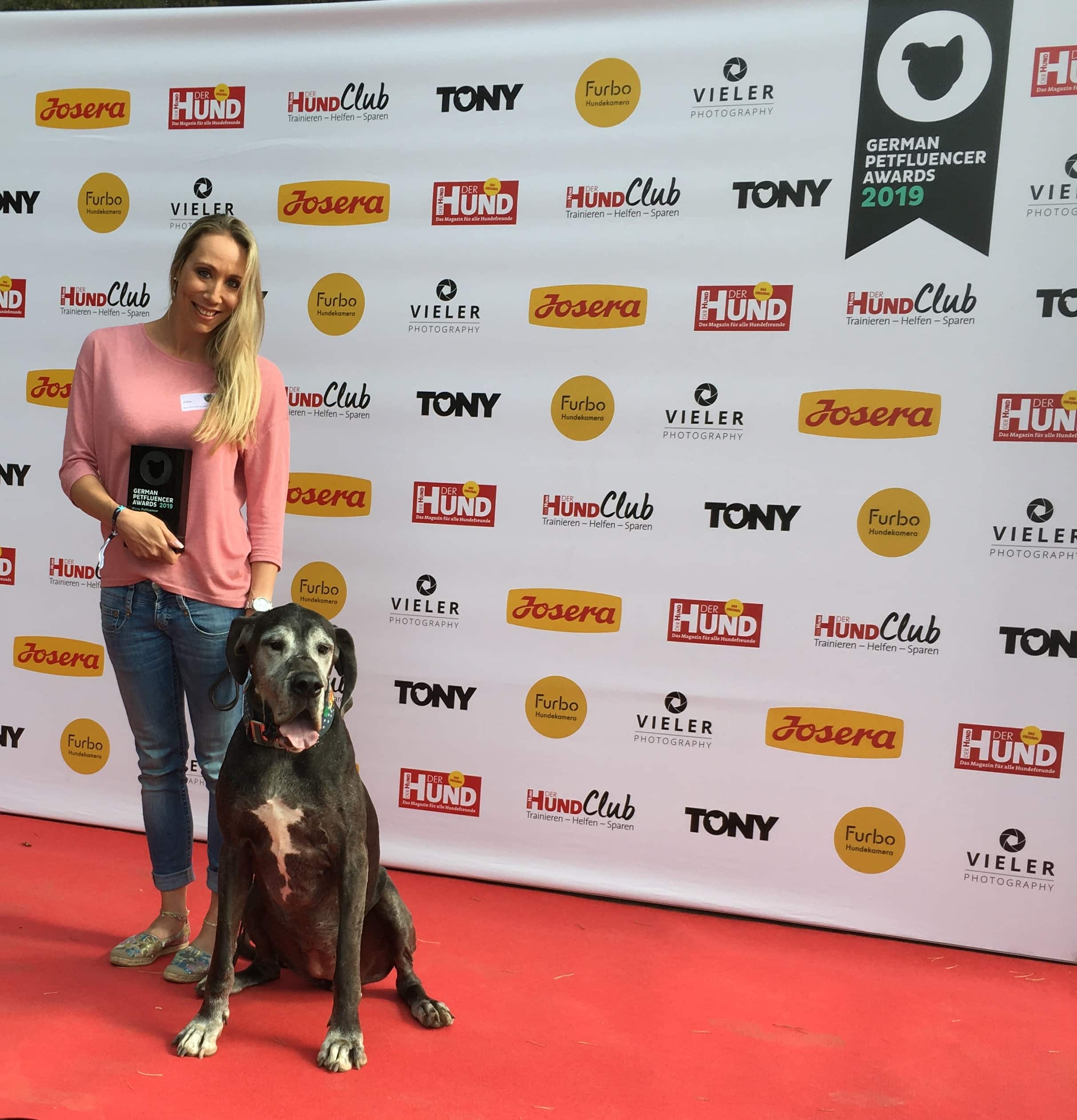 Frau mit großer schwarzer Dogge und Auszeichnung steht auf rotem Teppich vor Sponsorenwand