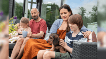 Eine Familie mit 2 Kindern und einem Dackel sitzen auf einem Outdoor-Sofa