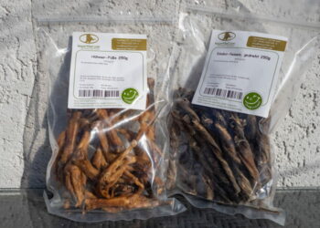 Eine durchsichtige Plastikverpackung mit Hühnerfüßen und eine Verpackung mit Rinder-Pansen-Stangen
