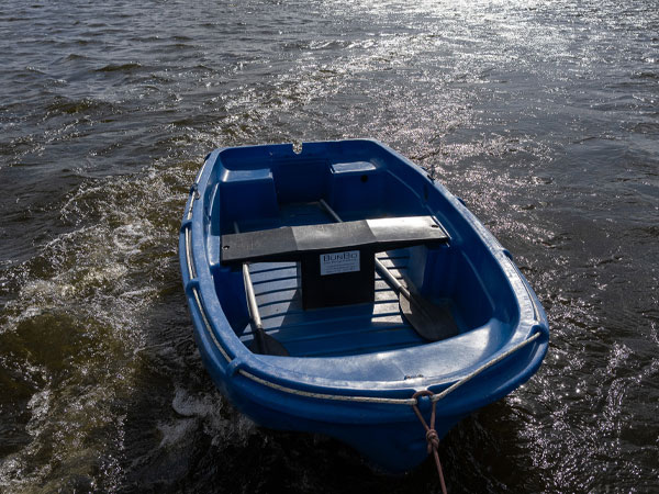 Kleines blaues Ruderboot schwimmt an einem Seil befestigt auf bewegtem Wasser in der Sonne.