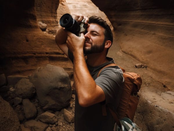 Person mit Rucksack fotografiert in einer felsigen Schlucht und hält die Kamera vor das Gesicht.