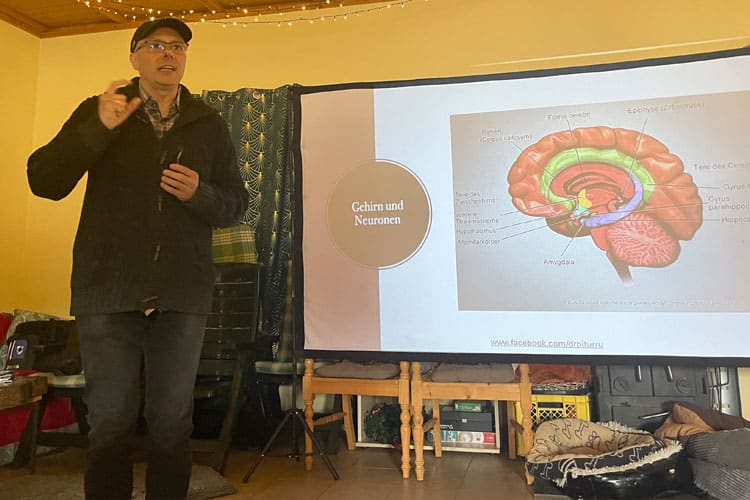 Pasquale Piturru spricht über das Gehirn und Neuronen, mit einer Gehirngrafik auf einer Leinwand.