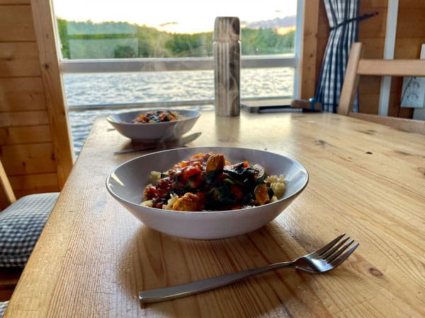 Zwei Schalen mit Pasta und Gemüse stehen auf Holztisch in Hausboot, See und Natur im Hintergrund.