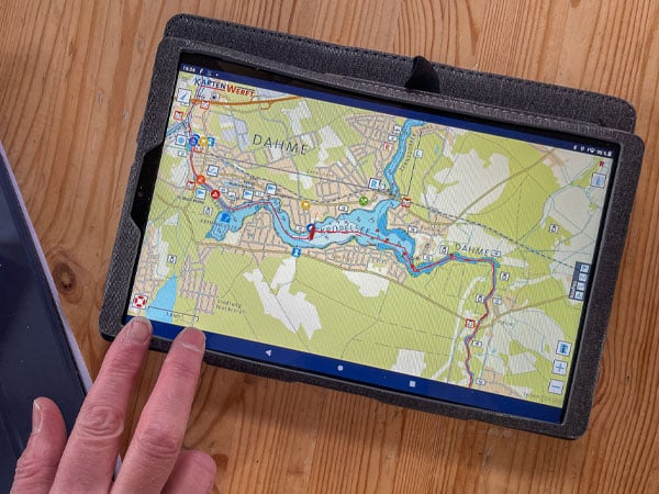 Tablet mit digitaler Gewässerkarte liegt auf Holztisch, eine Hand deutet auf den Bildschirm.