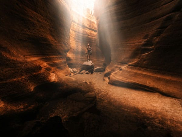 Person steht auf einem Felsen im Sonnenlicht in einer weitläufigen, orangefarbenen Felsschlucht.