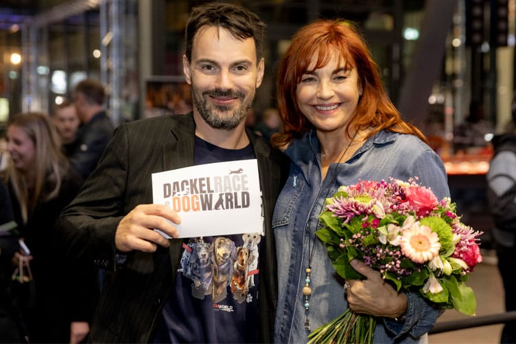 Person mit „Dackelrace DogWorld“-Schild und Diana Eichhorn mit Blumen auf der DogWorld München.
