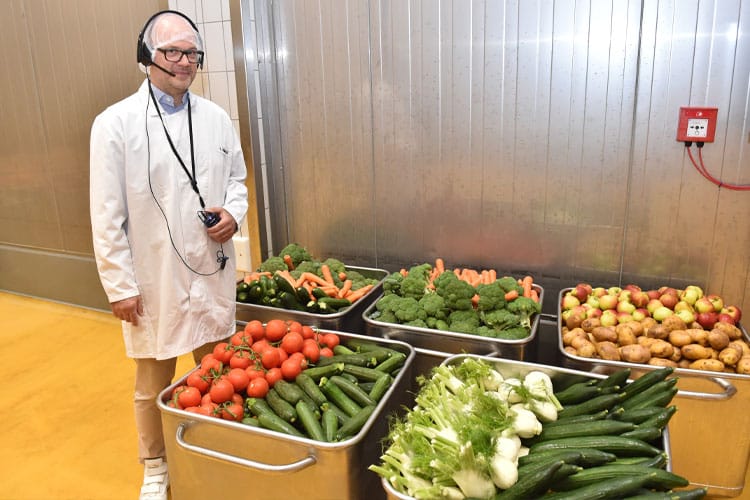 COO Thomas Reinarz steht neben Behältern mit frischem Gemüse und Obst wie Tomaten, Zucchini, Fenchel und Äpfeln.