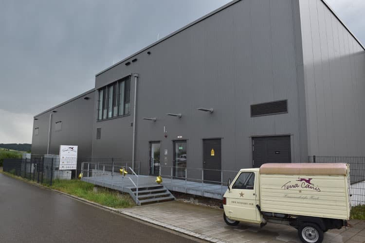 Graues Industriegebäude mit Rampe, davor steht ein kleines Lieferfahrzeug mit „Terra Canis“-Logo.
