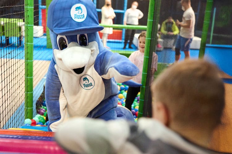 Maskottchen Flosse begrüßt ein Kind im bunten Abenteuerland des Club Aldiana.