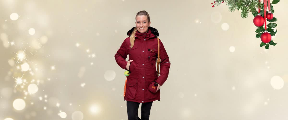 Person mit dunkelroter Winterjacke steht vor weihnachtlichem Hintergrund mit Lichtereffekten und Deko.