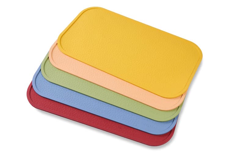 Fünf verschiedenfarbige, rechteckige Napfunterlagen liegen gestapelt auf weißem Hintergrund.