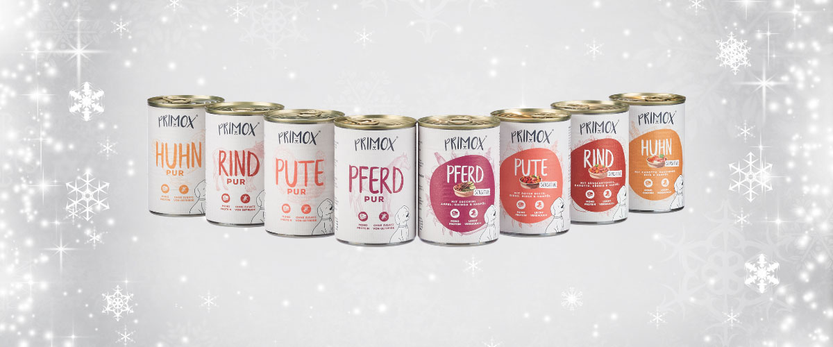 Verschiedene Sorten PRIMOX Hundefutter in Dosen stehen nebeneinander vor einem winterlichen Hintergrund mit Schneeflocken.