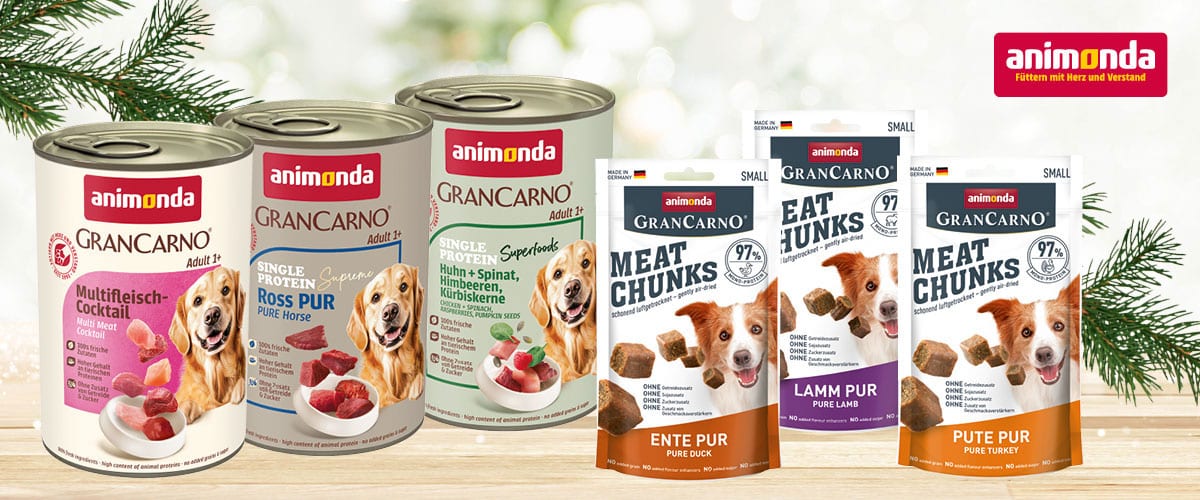 Verschiedene Animonda GranCarno Hundefutterdosen und Snackpackungen stehen nebeneinander auf einem Holztisch im Winterdekor.