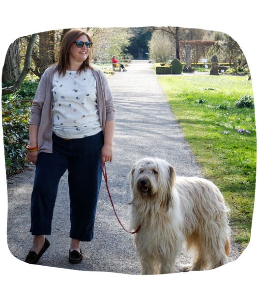 Nadine Dapra steht bei gutem Wetter neben ihrem langhaarigem Schafpudel-Mix Couscous auf einem Parkweg.