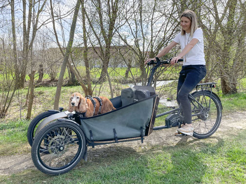 Redakteurin Vroni im Sattel des Lastenrads, Spaniel Barney steht in Transportbox