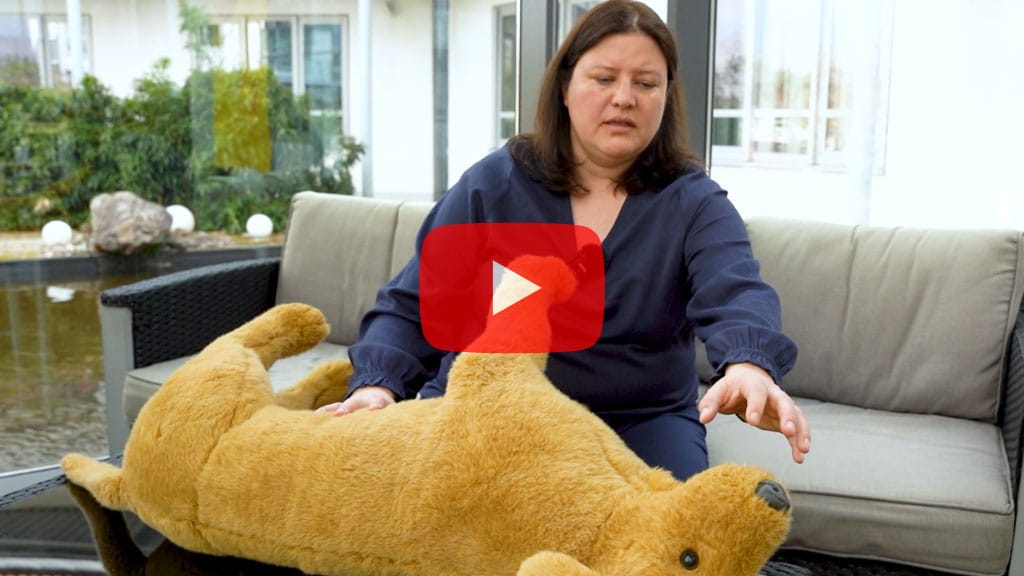 Nadine Dapra sitzt auf einem Sofa und hält einen großen Stoffhund, der auf der Seite liegt.