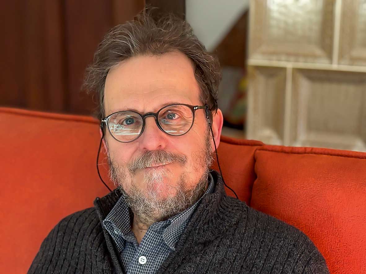 PD Dr. Udo Gansloßer sitzt auf einem orangeroten Sofa und schaut zur Kamera.